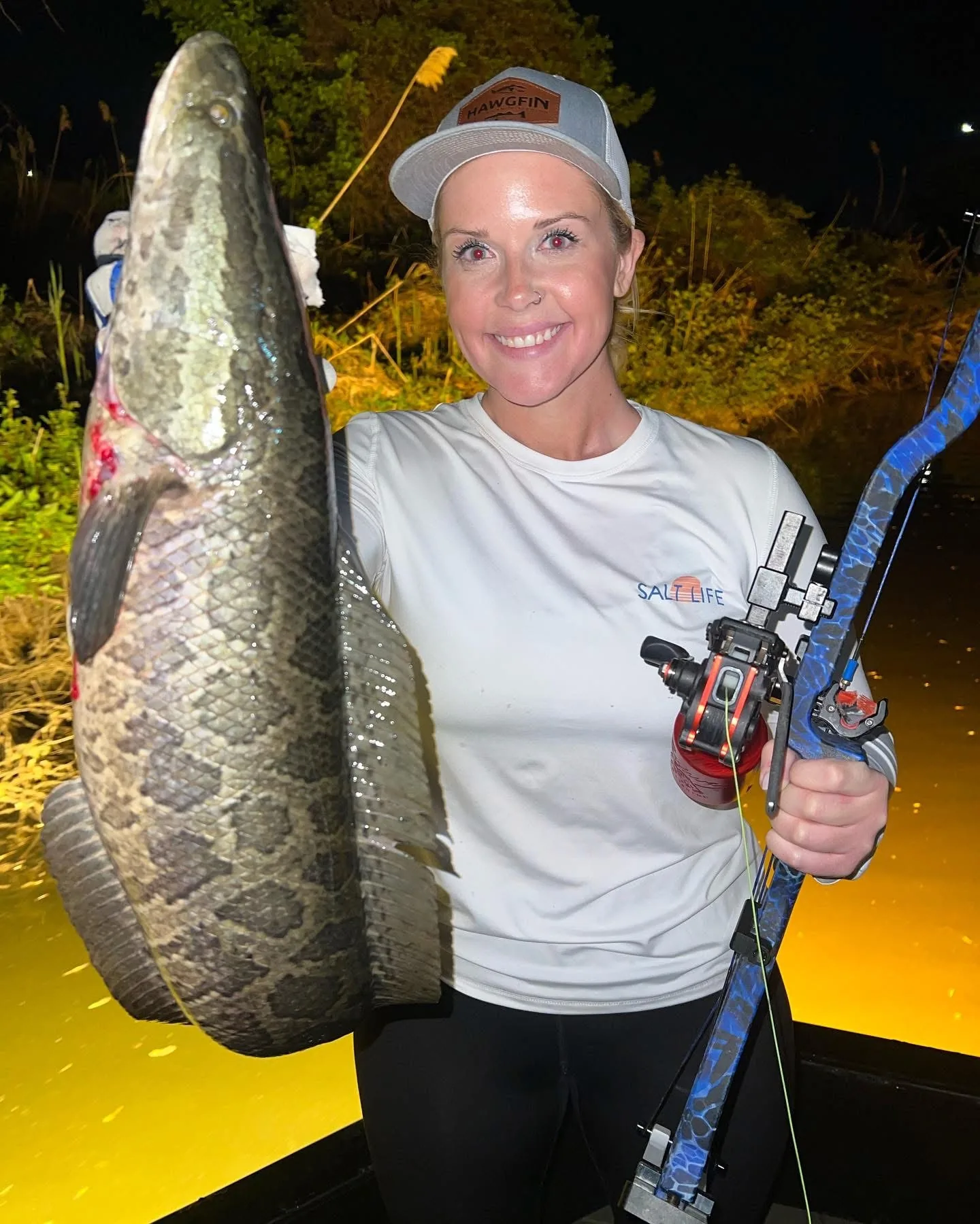 Guest holding a snakehead with bowfishing gear on a night charter