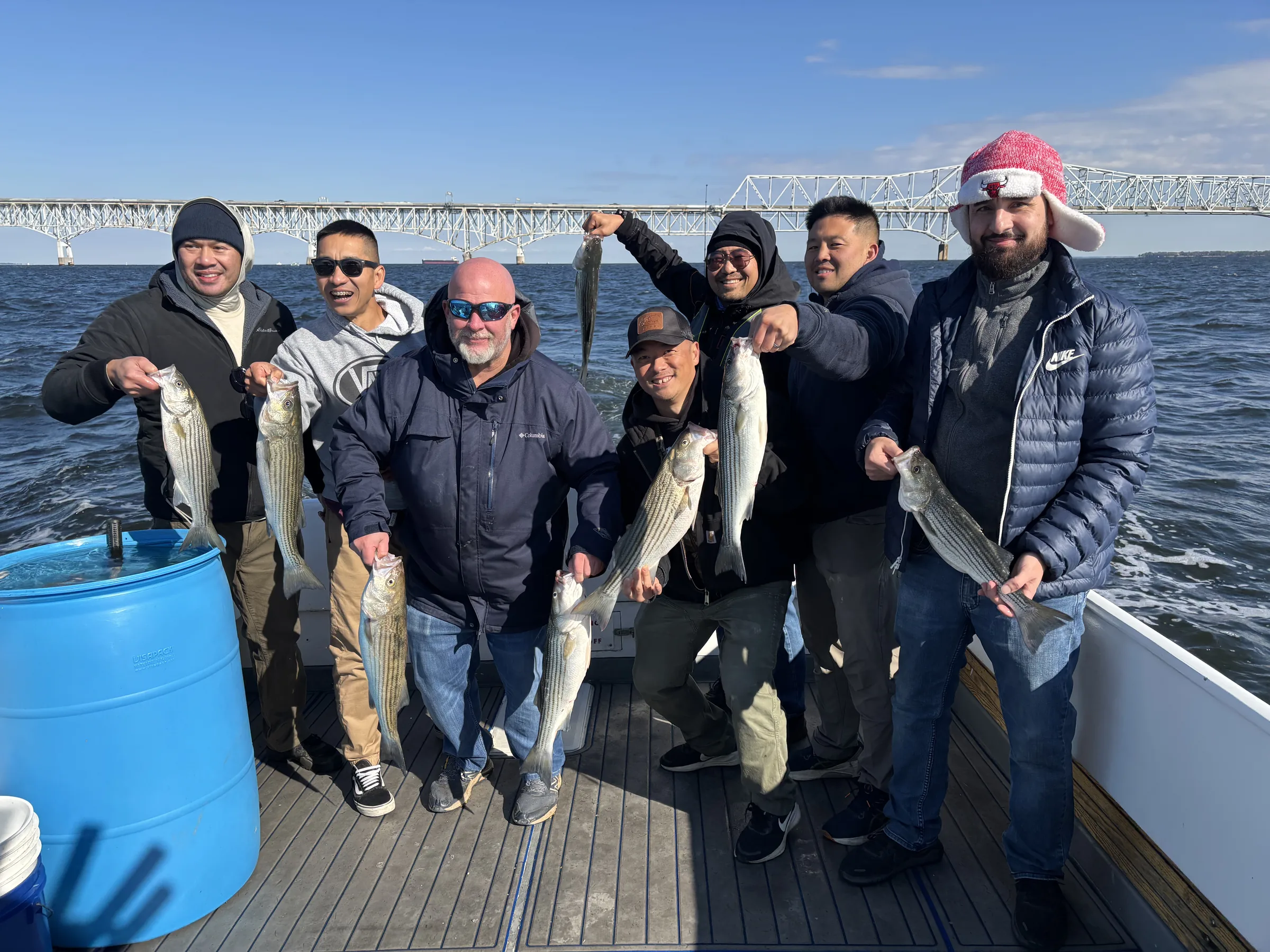 Mixed charter group holding rockfish with the Chesapeake Bay Bridge in the background